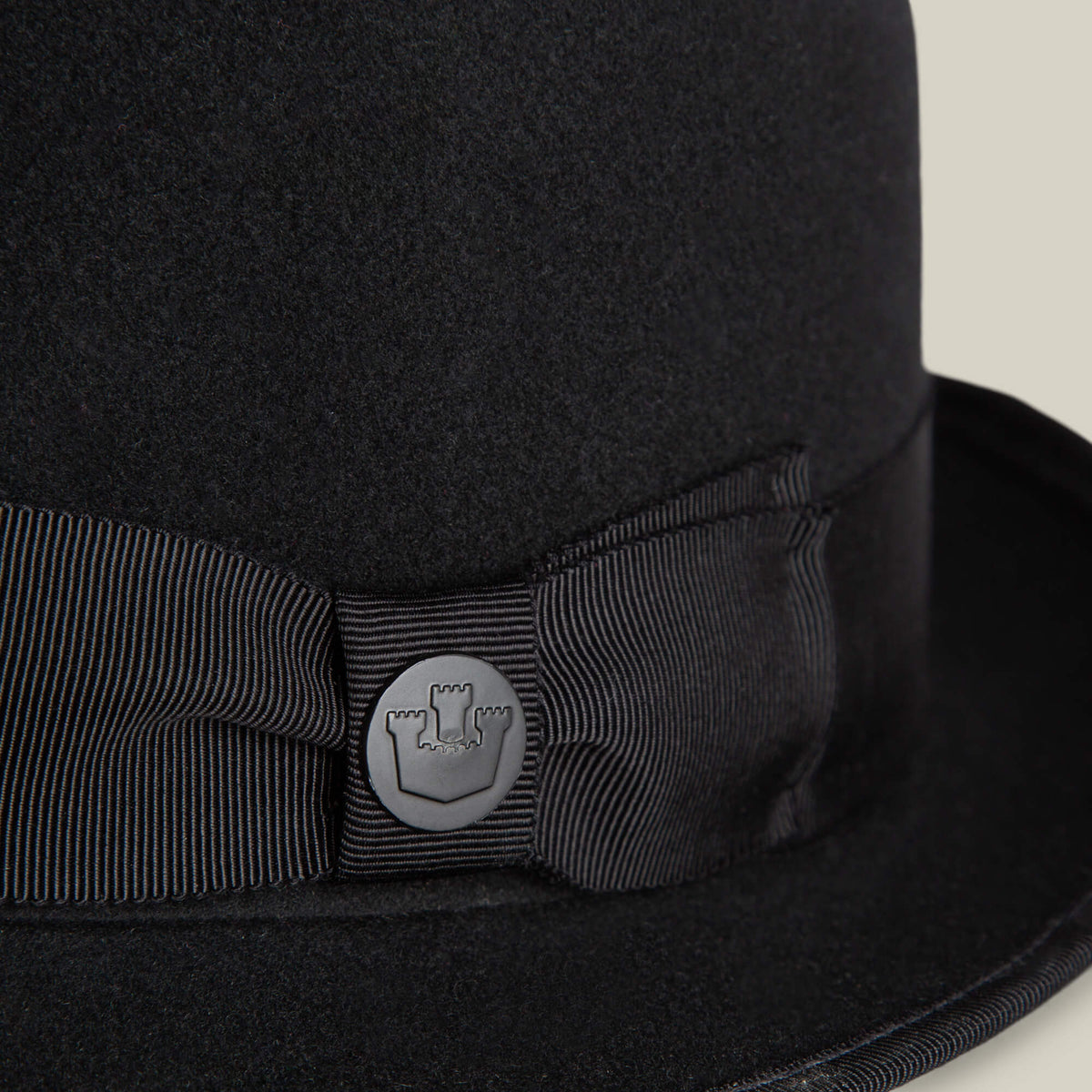 Close-up of the Slick Carter by Goorin Bros.: a black felt hat with a ribbon and round metal pin featuring a castle turret emblem, showcasing effortless style and a classic wool short brim design.