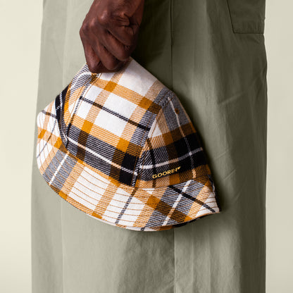 A person in light green pants holds the Bespoke Wordmark Bucket by Goorin Bros., a plaid hat crafted from soft cotton linen for a stylish and comfortable look.