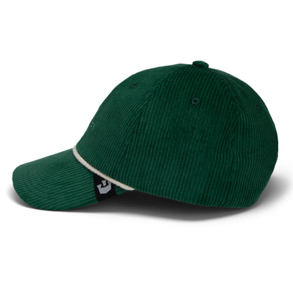 The Clubhouse by Goorin Bros. is a dark green wide wale corduroy baseball cap featuring a curved brim and white trim along the edge, shown from a side angle for an understated touch of quiet luxury.
