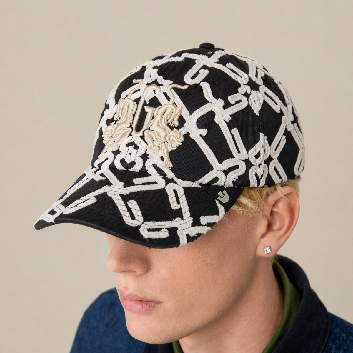 A person wearing the black and white "Future Baby Daddy" cap by Goorin Bros., featuring all-over embroidery, a blue jacket, and a small stud earring, viewed from a slightly elevated angle.