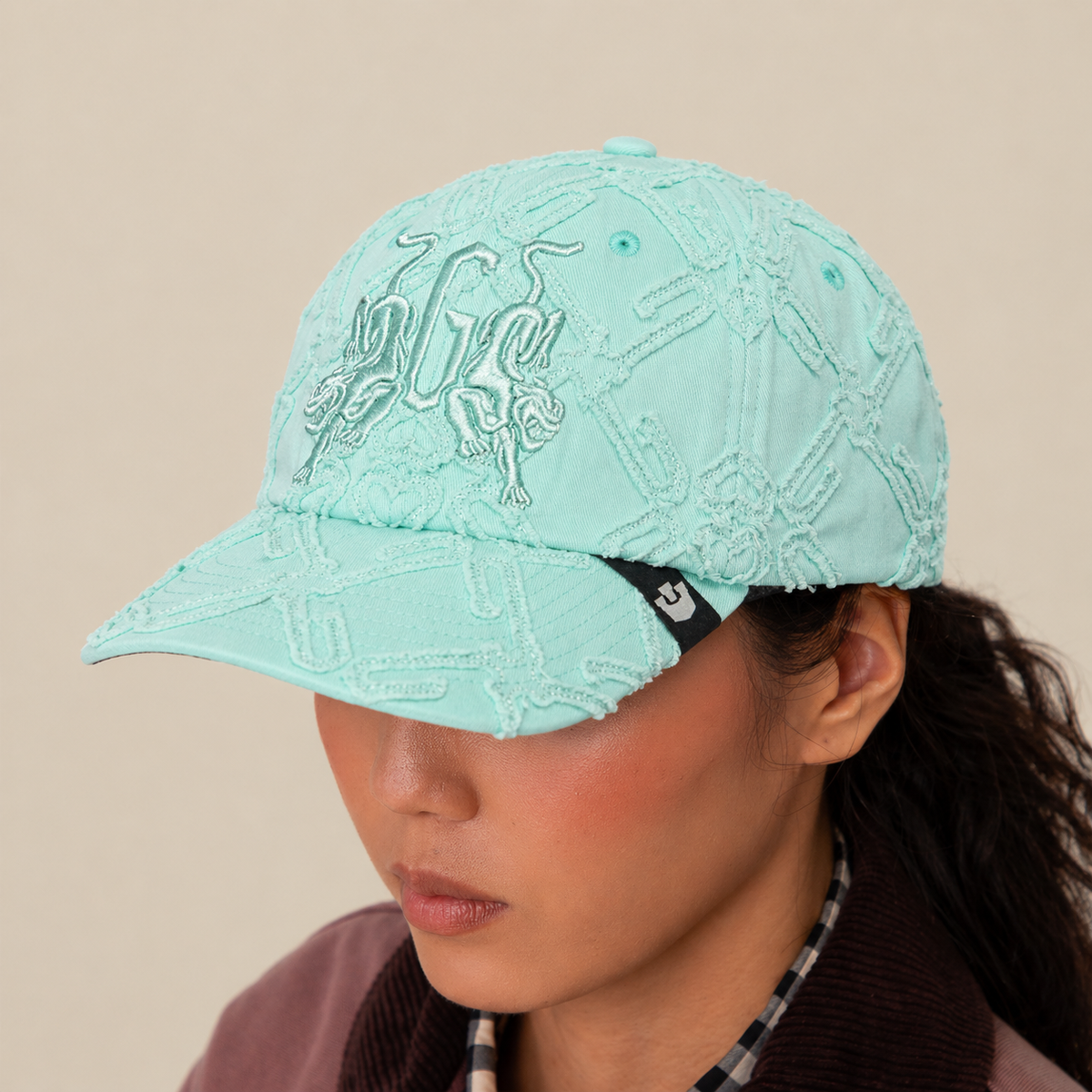 A person wears the Goorin Bros. "Future Baby Daddy" cap in light blue with all-over embroidery and a black tag, styled with a brown jacket and plaid shirt. The plain beige background highlights their main character energy.