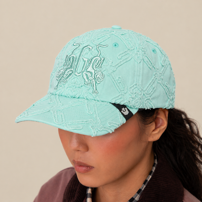 A person wears the Goorin Bros. "Future Baby Daddy" cap in light blue with all-over embroidery and a black tag, styled with a brown jacket and plaid shirt. The plain beige background highlights their main character energy.