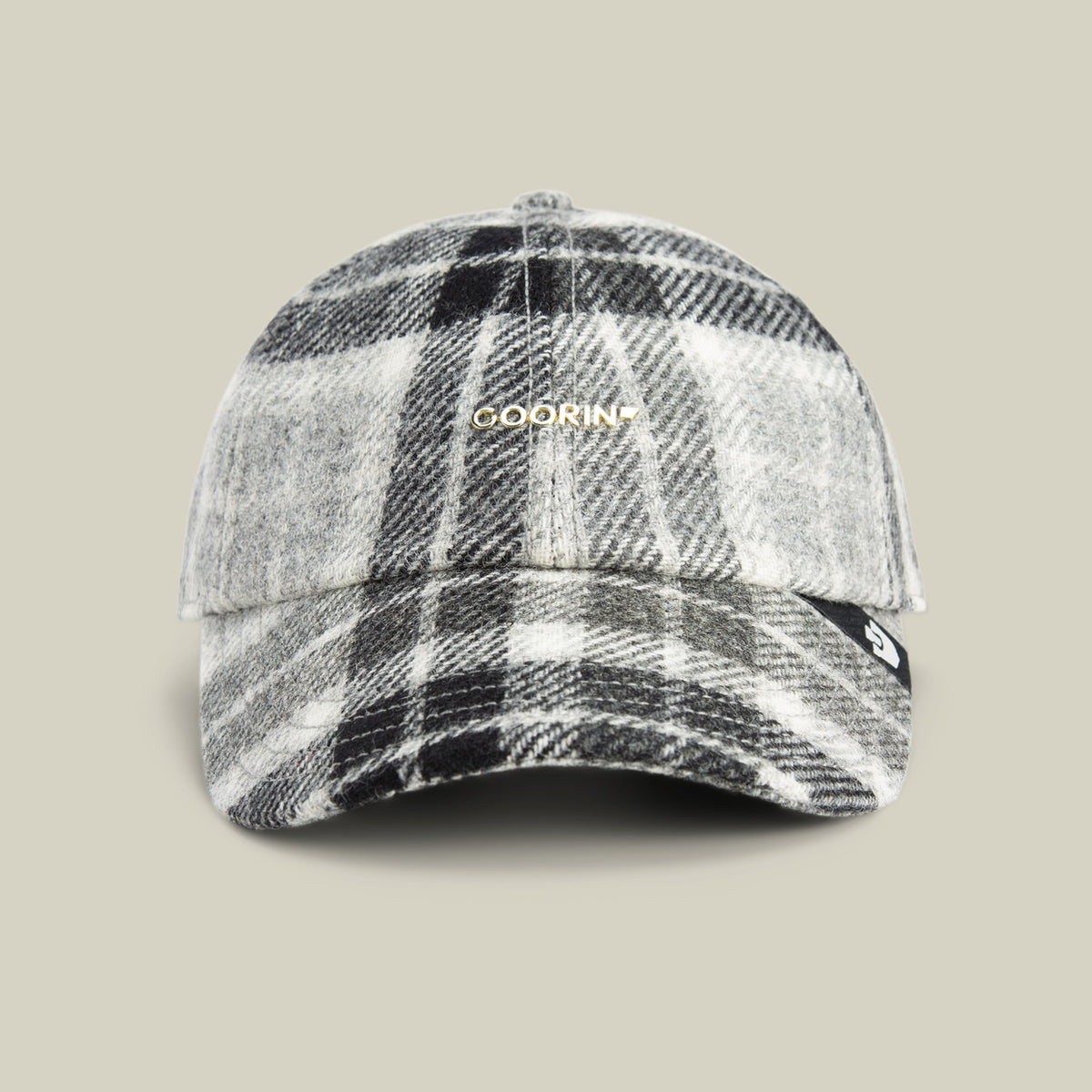 A black, white, and gray plaid wool blend baseball cap from Goorin Bros., featuring their “Bespoke Wordmark” in gold on the front, displayed against a plain beige background.