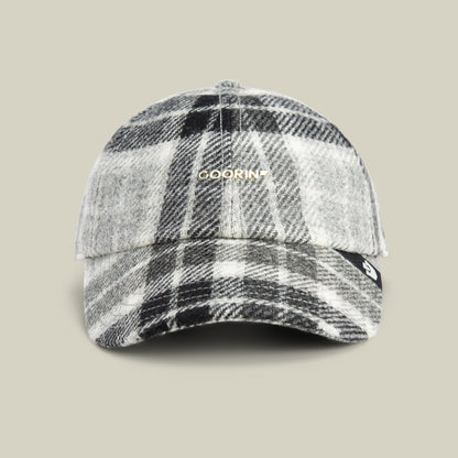 A black, white, and gray plaid wool blend baseball cap from Goorin Bros., featuring their “Bespoke Wordmark” in gold on the front, displayed against a plain beige background.