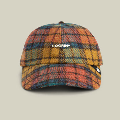 Introducing the Bespoke Wordmark cap by Goorin Bros.—a plaid wool blend baseball cap in vibrant orange, yellow, blue, and green hues. This modern heritage design features a curved brim, a bespoke GOORIN wordmark prominently on the front, and a small side tag for an added touch of distinction.