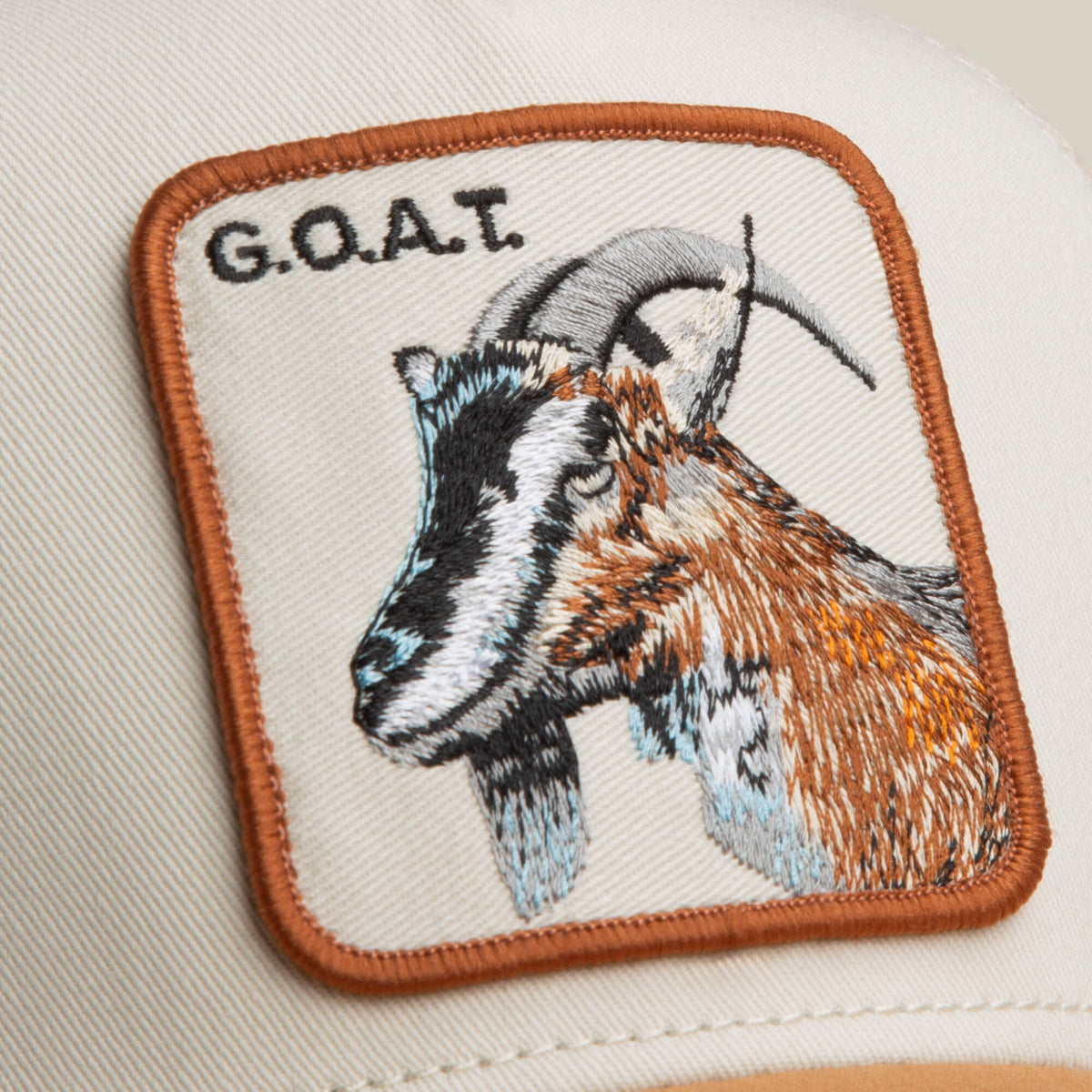 The Goat Trucker by Goorin Bros. features a bold neutral-toned patch with an embroidered goat head and "G.O.A.T." in uppercase letters above the image.
