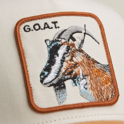 The Goat Trucker by Goorin Bros. features a bold neutral-toned patch with an embroidered goat head and "G.O.A.T." in uppercase letters above the image.