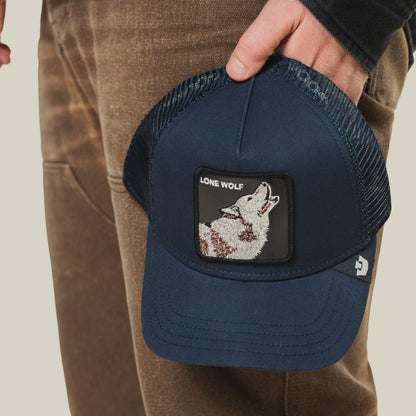 A person holds the Lone Wolf Trucker hat by Goorin Bros., featuring a navy blue design with a wolf patch and "LONE WOLF" embroidered on the front, exuding true outlaw energy.