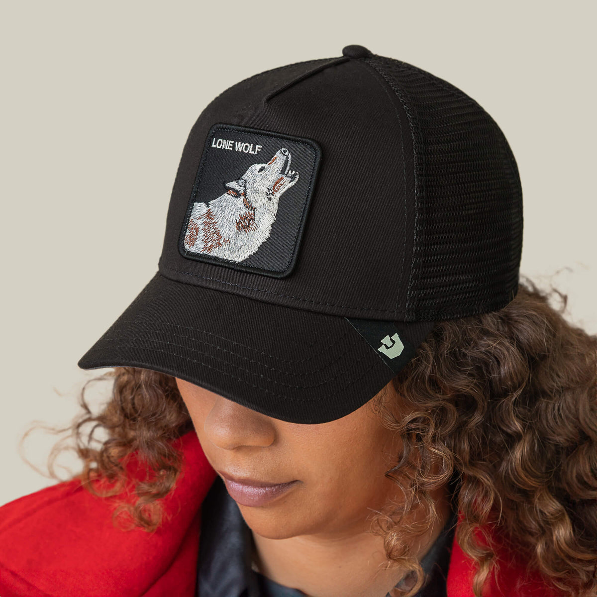 Wearing the Goorin Bros. Lone Wolf Trucker, a black hat featuring a howling wolf patch and “Lone Wolf,” this person in a red jacket gazes downward, radiating unmistakable outlaw energy.