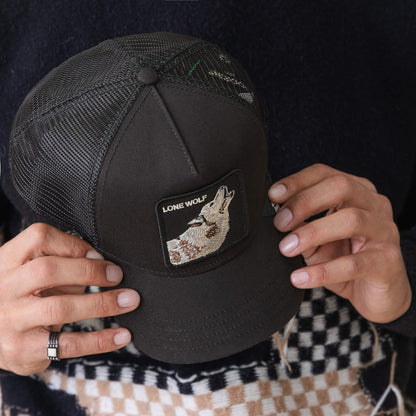 Person holding the Goorin Bros. Lone Wolf Trucker, a black mesh hat with an embroidered patch of a howling wolf and "LONE WOLF" on the front.