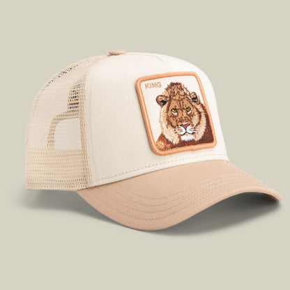 The Goorin Bros. King Trucker cap features beige and tan panels, a mesh back, and a front patch with an embroidered lion head and "KING" text.