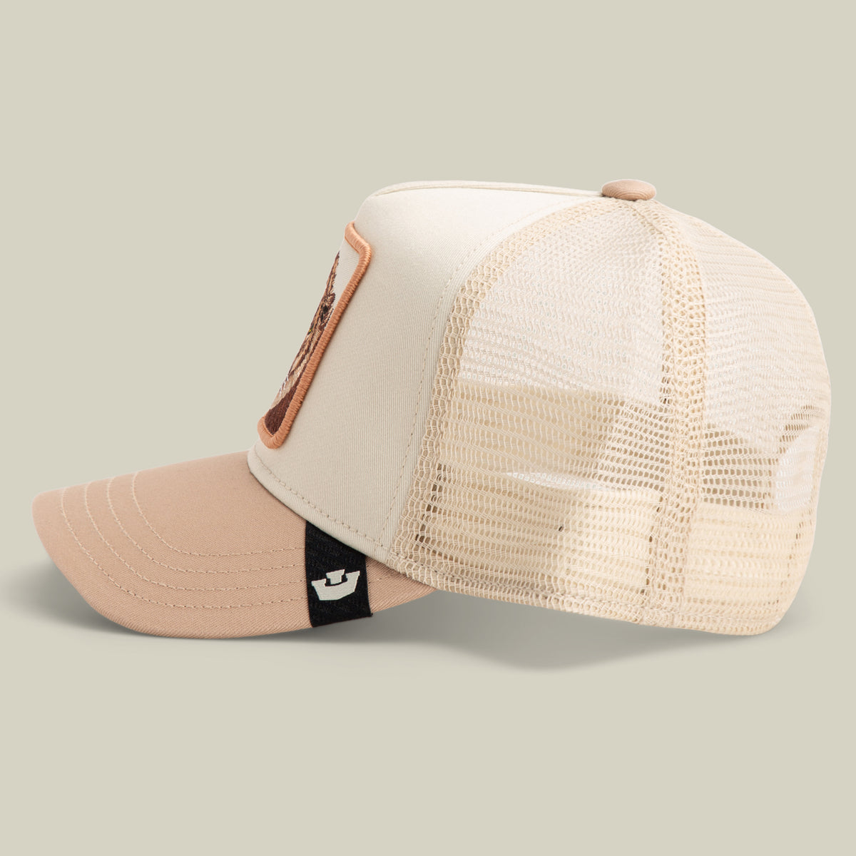 The Goorin Bros. King Trucker is a beige and tan hat featuring a mesh back, curved brim, and a front patch, displayed in side profile.