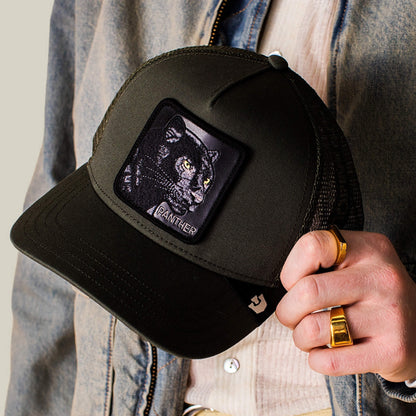 A person holds the Panther Trucker hat by Goorin Bros.—a black mesh trucker style featuring a front patch with an embroidered black panther and the word PANTHER.