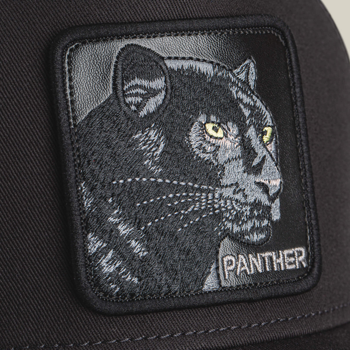 Close-up of the Goorin Bros. Panther Trucker hat with a black patch, featuring an embroidered panther head with yellow eyes and "PANTHER" stitched below.