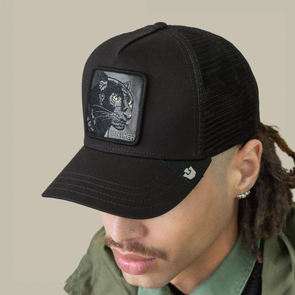 A person sports the Goorin Bros. Panther Trucker—a black mesh baseball cap featuring a stitched panther patch—paired with a green collared shirt and jacket.