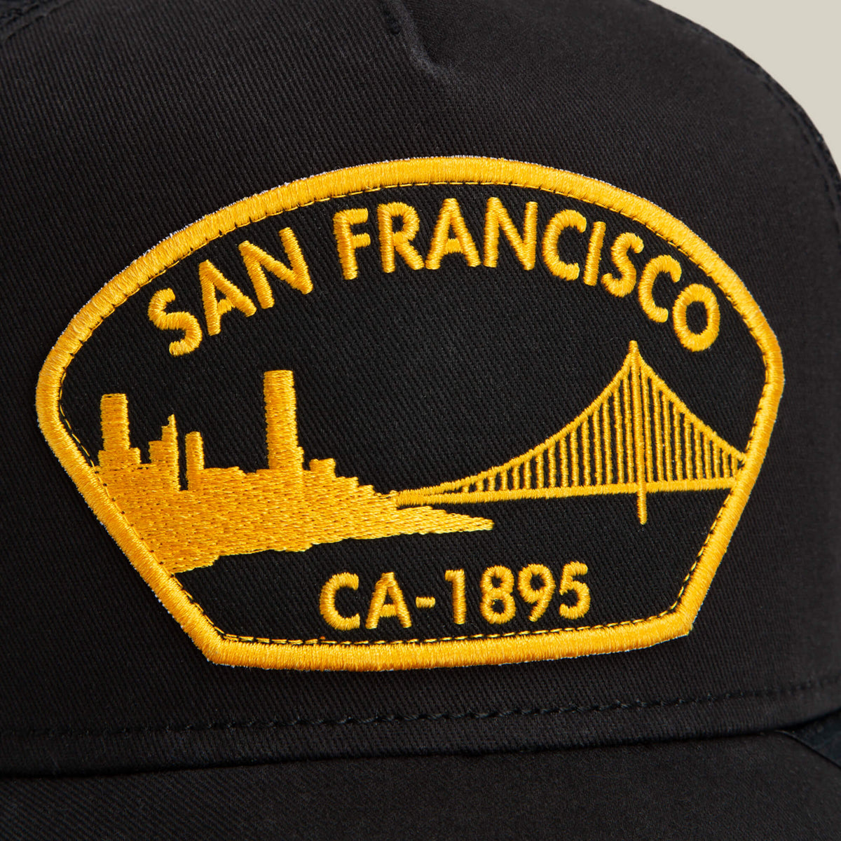 A black Goorin Bros. cap named "San Francisco" features a yellow embroidered patch with "San Francisco CA-1895" and images of a city skyline and bridge.