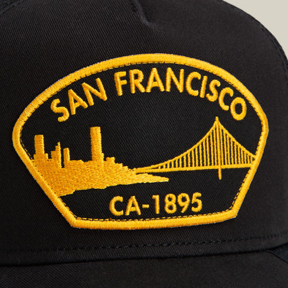 A black Goorin Bros. cap named "San Francisco" features a yellow embroidered patch with "San Francisco CA-1895" and images of a city skyline and bridge.