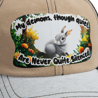The Goorin Bros. Lil Ronin tan cap from our Storybook collection has white stitching and a patch with a gray rabbit and the words, “My demons, though quiet, are never quite silenced.”.