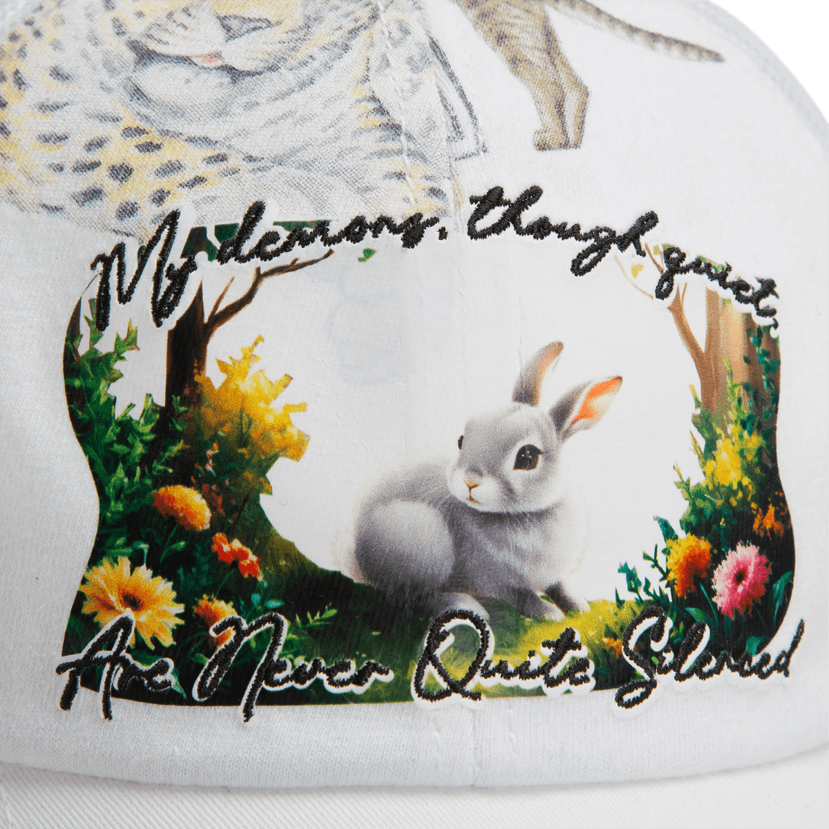 Close-up of a white fabric from Goorin Bros.' Lil Ronin collection, featuring a printed rabbit, floral accents, and the embroidered text: My demons, though quiet, are never quite silenced.