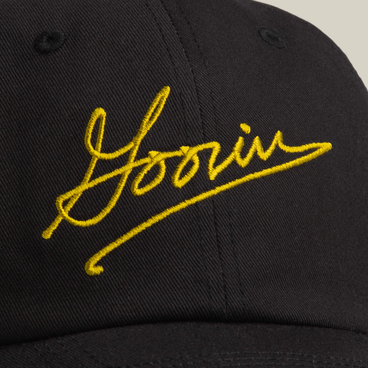 A close-up of the Goorin Script Papa cap by Goorin Bros., featuring black fabric and "Yoorin" embroidered in yellow script on the front, inspired by classic Goorin styles.