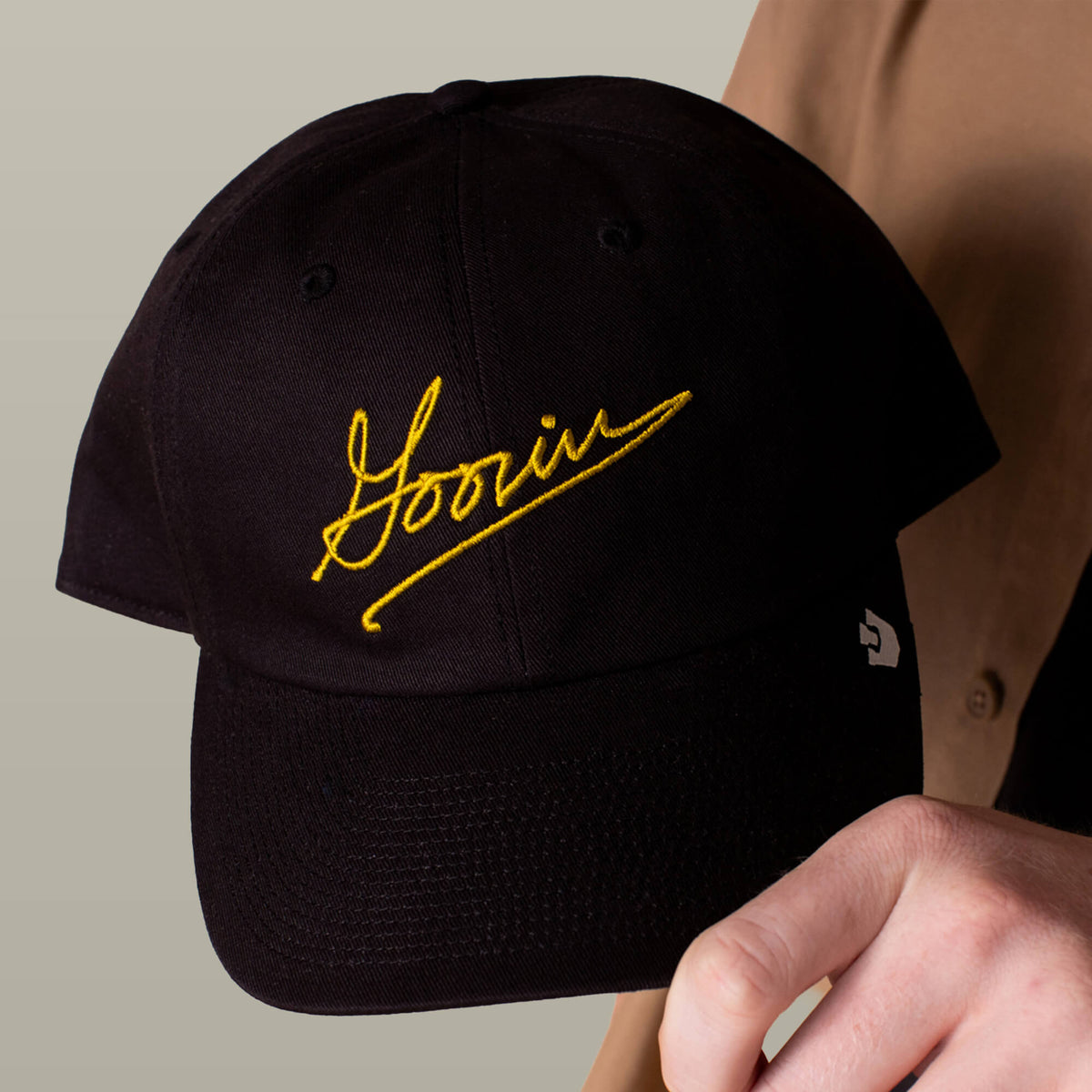 A person holding the Goorin Bros. Goorin Script Papa cap, featuring yellow script embroidery on the front.