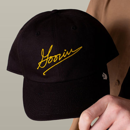 A person holding the Goorin Bros. Goorin Script Papa cap, featuring yellow script embroidery on the front.