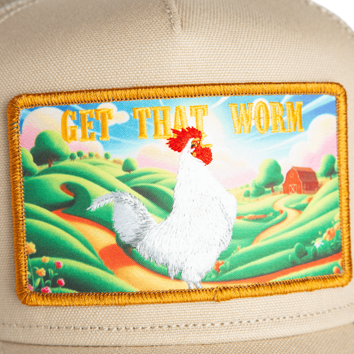 A close-up of the Greener Grass - Get that Worm trucker hat by Goorin Bros., showing a fabric patch with a white chicken, scenic farm landscape, and "GET THAT WORM" in bold yellow on beige.