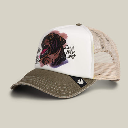 The Bad Boy Disruption trucker hat by Goorin Bros. features a hand-illustrated Rottweiler insignia on a white front panel, olive green bill, and beige mesh back, with "IM A BAD BOY" text for bold attitude.
