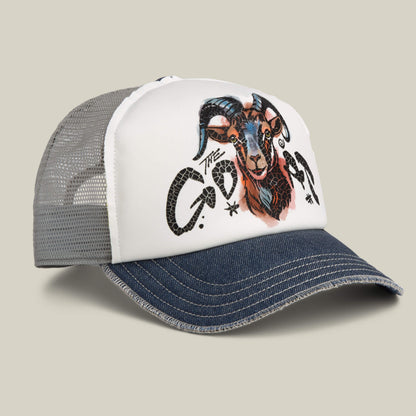 The Goat Disruption trucker hat by Goorin Bros. features a denim bill, white front with a hand-illustrated goat head and "THE GOAT" text, plus a breathable mesh back.