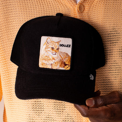 A person in a beige sweater holds Goorin Bros.' Terry Cloth Cat—a plush black terry cloth cap featuring an embroidered cat patch and the word BOUJEE, exuding effortless luxury and lounge-level softness.