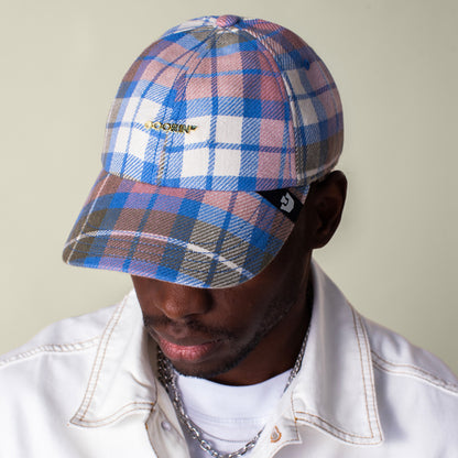 A person in a white jacket looks down, their face partially shaded by the brim of the Bespoke Wordmark V2 papa cap by Goorin Bros., featuring pink, blue, and white plaid cotton linen and a GOORIN wordmark.