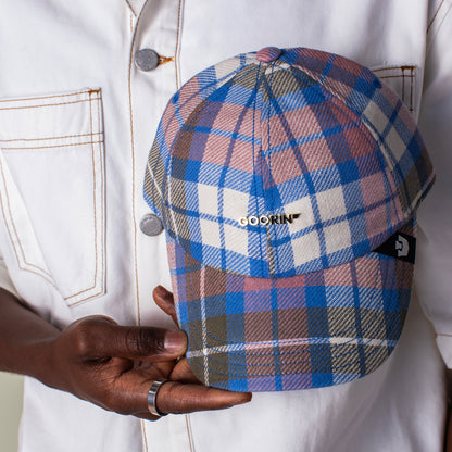 A person in a white jacket holds a Bespoke Wordmark V2 plaid cap by Goorin Bros., showcasing the stylish cotton linen papa cap design with the distinctive GOORIN branding on the front.