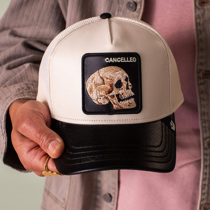 A person holds the Goorin Bros. Faux Leather Skull hat in beige and black, featuring a skull patch with "CANCELLED" above it.