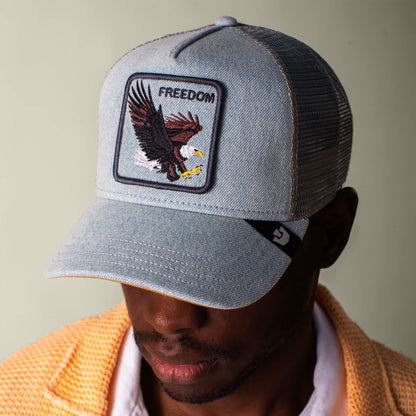 A man wears the Goorin Bros. Denim Eagle light blue baseball cap with an eagle patch and "FREEDOM" on front, styled with a yellow textured jacket over a white shirt.