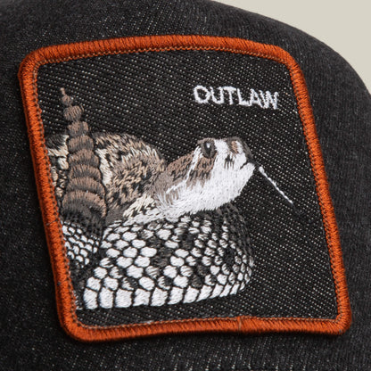 A close-up of the Goorin Bros. Denim Snake cap reveals a black denim design with an embroidered rattlesnake patch and the word OUTLAW in white, accented by orange stitching.