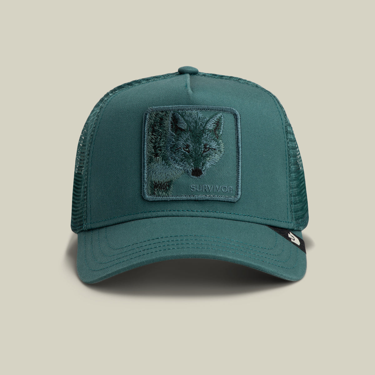 The Goorin Bros. Mirage Survivor trucker hat in SEA features mesh sides and a bold front patch with a wolf face and the word “SURVIVOR.”.