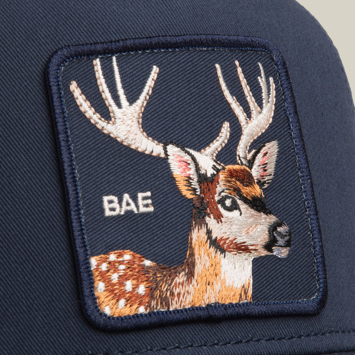 Close-up of the Goorin Bros. Mirage Bae patch in navy blue, styled like a classic trucker, featuring an embroidered antlered deer and the word “BAE” stitched alongside.