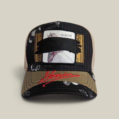 The Goorin Bros. Goorin Rework Trucker in VOID features a mesh back, ID card patch front, black strap detail, red embroidery, and paint splatter accents—available as a limited edition.