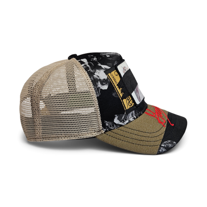 Side view of the Goorin Rework Trucker by Goorin Bros., a limited edition trucker hat with a mesh back, black and olive green floral-patterned fabric, decorative patches, and red embroidery on the brim.