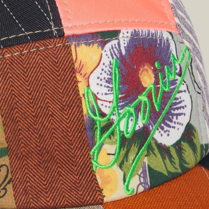 A close-up of the Goorin Bros. Goorin Rework Camper, a limited edition patchwork fabric hat with multicolored patterns, a flower design, and neon green Goorin embroidery.