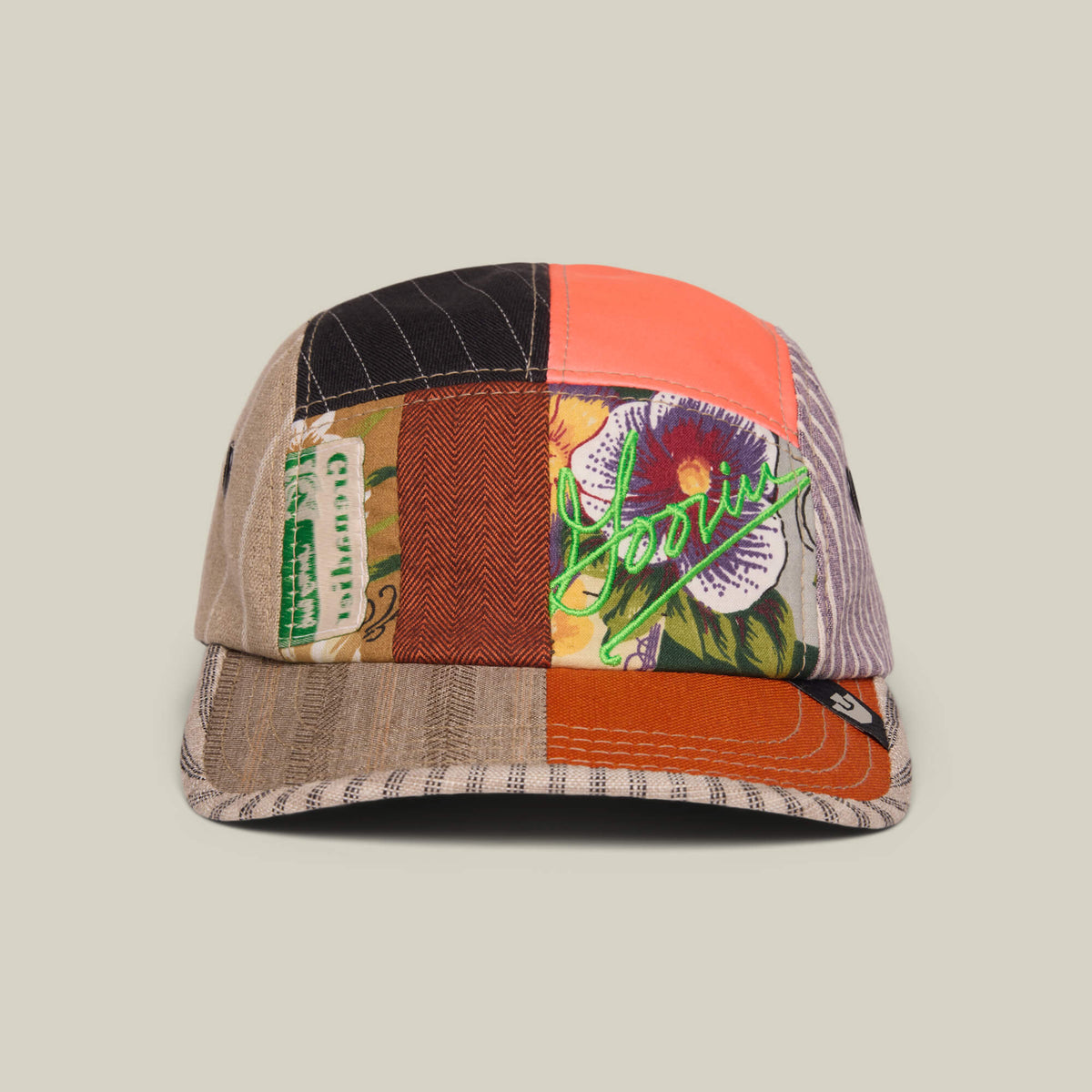 The Goorin Bros. Goorin Rework Camper in BISCUIT is a limited edition, multicolored recycled camp cap with patchwork patterns, floral details, green script embroidery, and a small label on the brim, shown against a plain background.