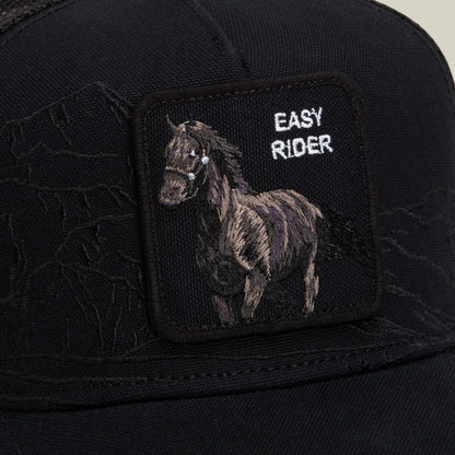 Goorin Bros. Badlands Stallion black cap featuring a patch with an embroidered horse and the words EASY RIDER in white lettering. Subtle mountain outlines appear in the background of the fabric.