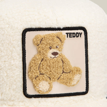 The Double Stuffed - Teddy trucker hat by Goorin Bros. features a cream-colored sherpa fabric adorned with a square patch on the top right, showcasing an embroidered brown teddy bear and the word "TEDDY" in black text, making this cozy accessory both charming and stylish.