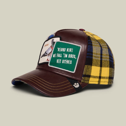 The Goorin Bros. Bird! trucker hat features a burgundy leather front with a green patch reading "Round Here We Ball, Em Birds, Not Bitches," paired with a yellow and navy plaid fabric back, shown against a neutral studio background.