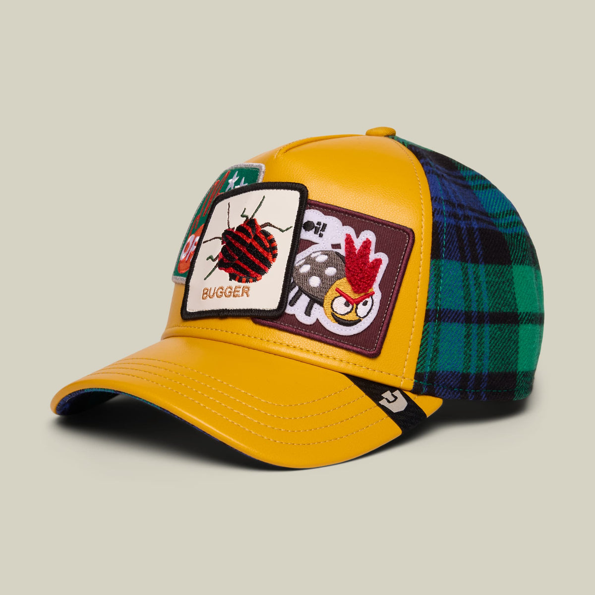 The Goorin Bros. Bugger yellow trucker hat features embroidered patches with a red ladybug and rooster design, green and navy plaid fabric on the back panels, and navy blue trim.