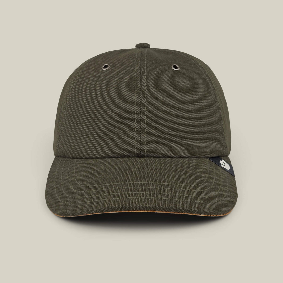 A front view of the Goorin Bros. Mineral Road baseball cap in olive green, featuring mixed materials, two metal eyelets, and a small black tag on the brim, hand cut and sewn, shown against a plain beige background.