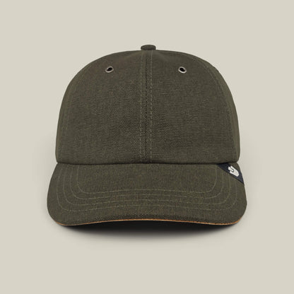 A front view of the Goorin Bros. Mineral Road baseball cap in olive green, featuring mixed materials, two metal eyelets, and a small black tag on the brim, hand cut and sewn, shown against a plain beige background.