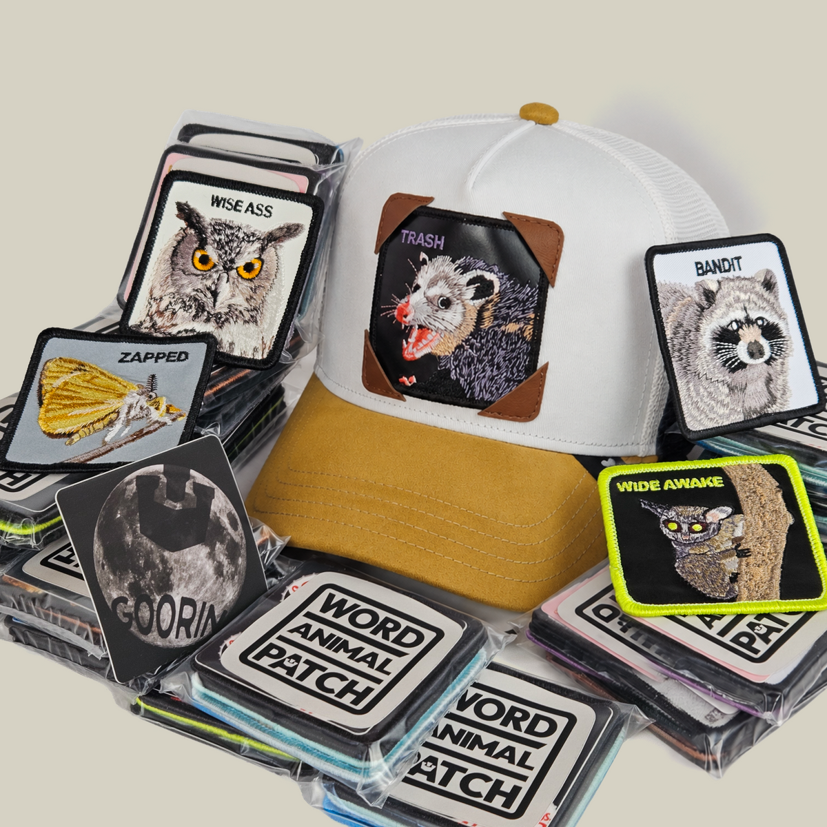 A white and tan Nocturnal Patch Pack with GB Patch Corner Trucker hat featuring an opossum patch, surrounded by a stack of Nocturnal Pack animal patches.
