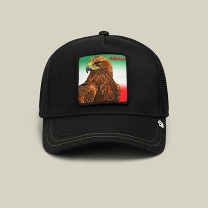 The Metallic Gradient Aguila by Goorin Bros is a black trucker hat featuring an embroidered eagle patch with Mexican flag colors on the front and mesh back panels.