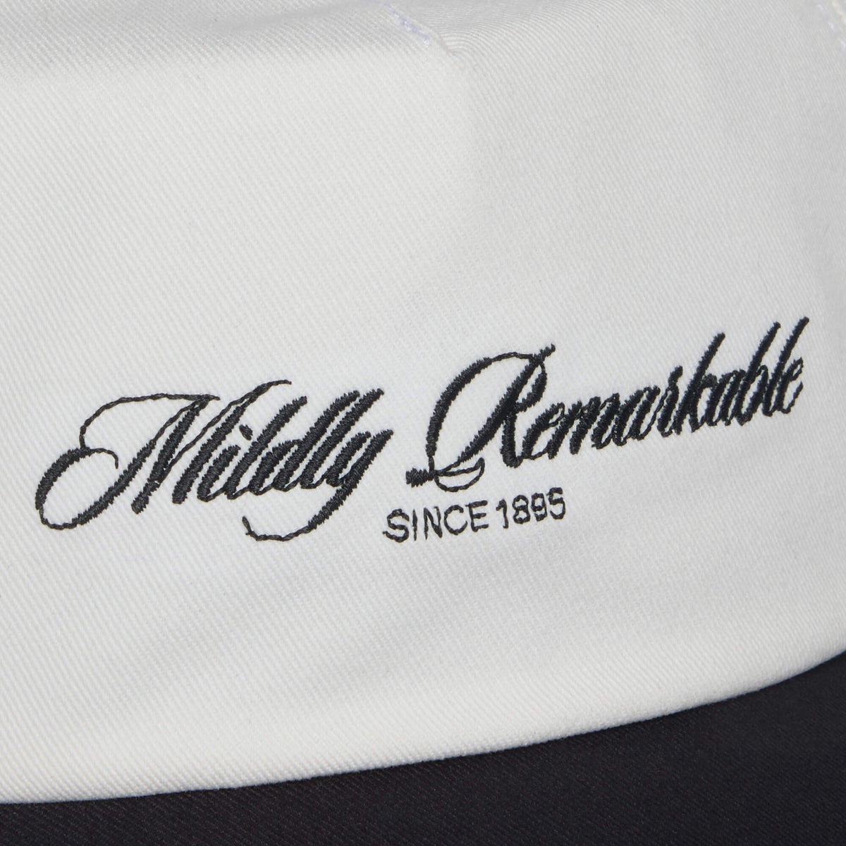 Close-up of white fabric featuring the Goorin Bros. Mildly Remarkable Script embroidery, "Mildly Remarkable SINCE 1895," evoking the timeless style of a classic Scrip hat.